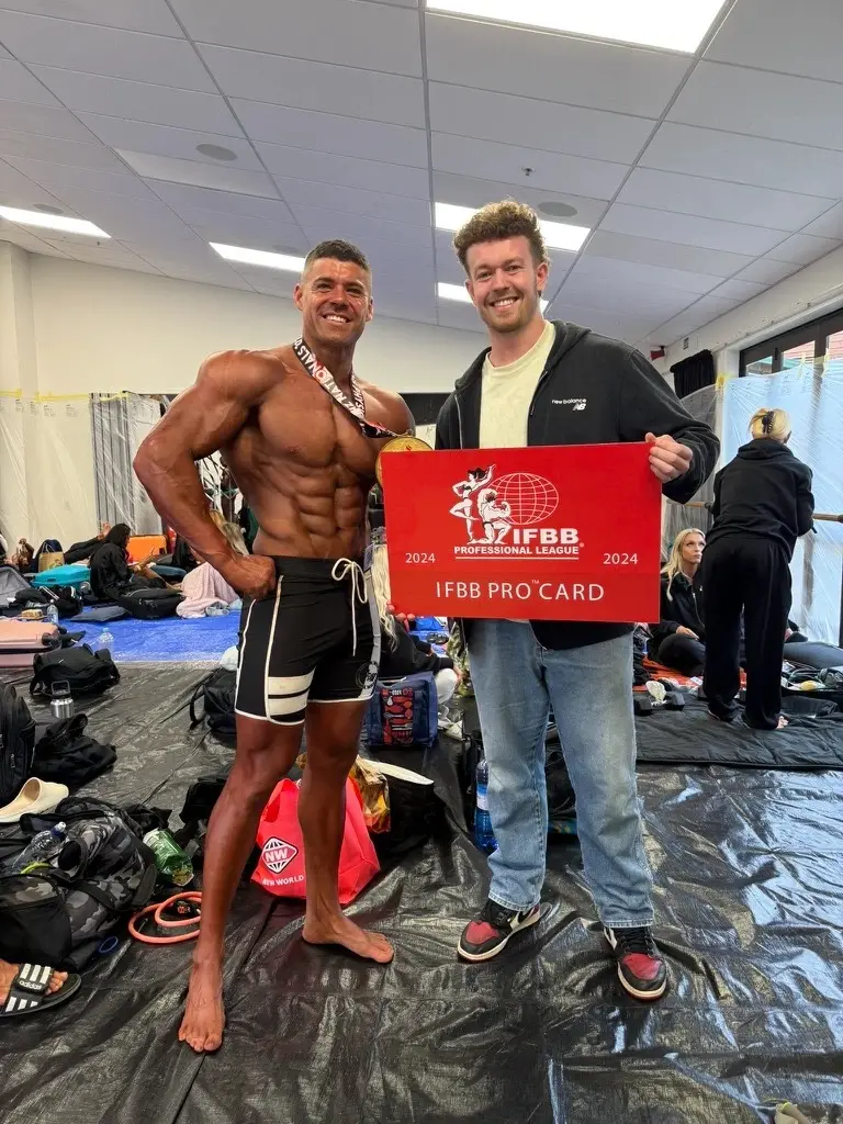 James holding an IFBB Pro Card with his athlete backstage